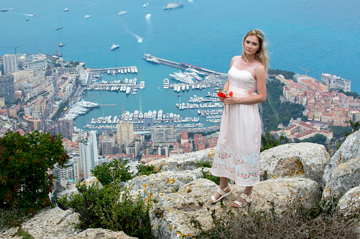 Pretty Young Blonde Woman In Gorgeous Pink Dress. Beautiful Aerial View of Monaco in The Background