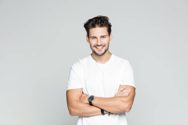 Young man standing confidently Portrait of attractive young caucasian man over grey background. Male model standing with his arms crossed and smiling. macho photos stock pictures, royalty-free photos & images