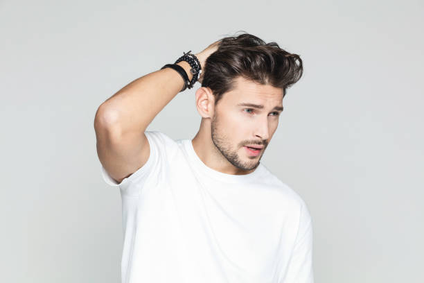 Stylish man posing on grey background Portrait of handsome male model posing with hand in hair and looking away against grey background. handsome people stock pictures, royalty-free photos & images