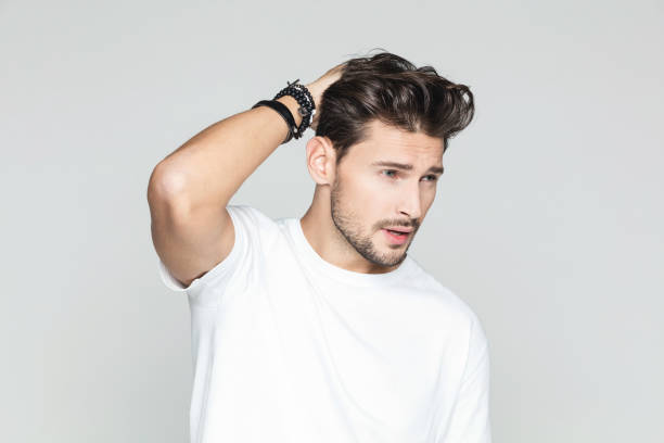 Stylish man posing on grey background Portrait of handsome male model posing with hand in hair and looking away against grey background. modelang stock pictures, royalty-free photos & images