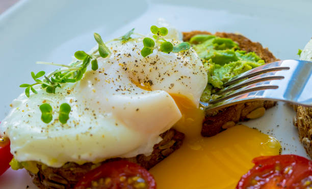 Close Up Poached Egg on Toasted Rye with Runny Yolk Poached egg on Toated Rye bread being cut up revealing a runny yolk, cress on top, tomatoes, egg cherry tomato rye stock pictures, royalty-free photos & images