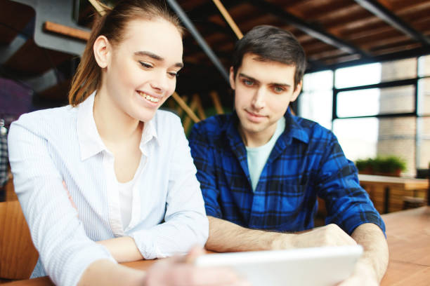 istock Casual young man and woman sharing tablet computer while sitting at table in daylight. 973489238