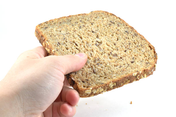istock Man's hand holding a slice of whole wheat bread 973498400