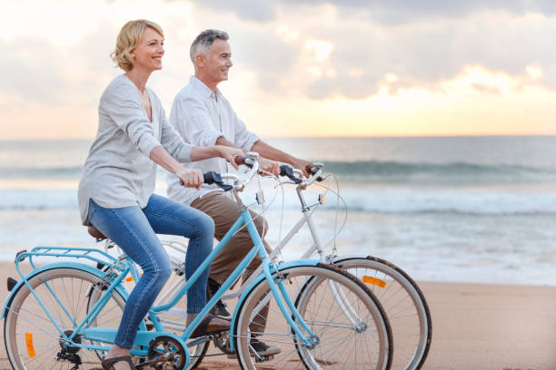 成熟したカップルがビーチで夕日や日の出サイクリングします。 - retirement mature couple couple bicycle ストックフォトと画像