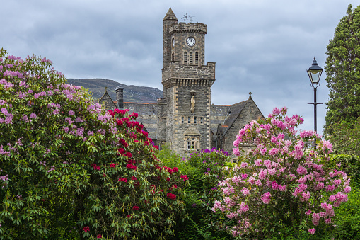 Fort Augustus, Scotland - June 11, 2012: Closeup of the Abbey Highland Club clock tower with flowers fronted by garden  under heavy cloudscape.