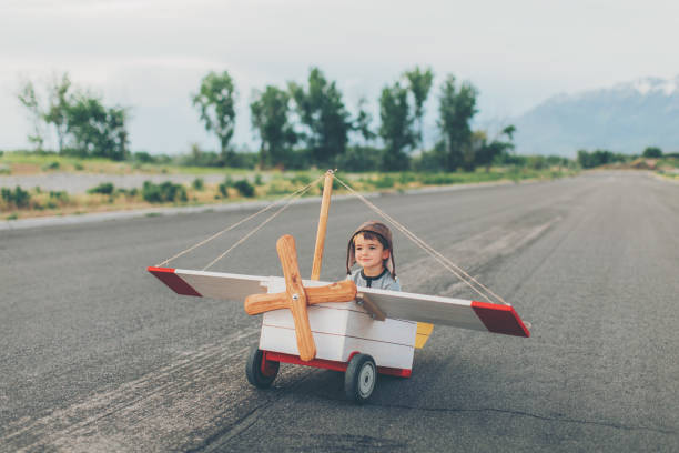 A young boy dressed in a flight cap gets ready to fly a vintage toy airplane. He is sitting in the plane as the pilot. Seeing sights from the sky has never been better. The boy is smiling and looking away from the camera. Image taken in Utah, USA.