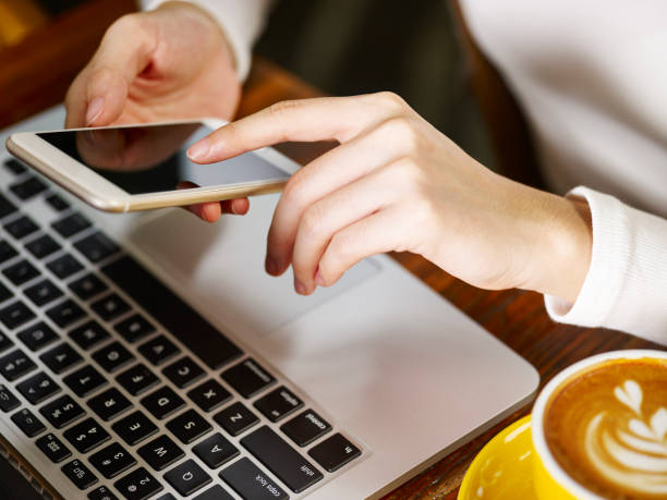 istock woman using cell phone and laptop in coffee shop 973629084