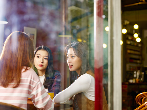 three happy beautiful young asian women sitting at table chatting talking relaxing in coffee shop or tea house.
