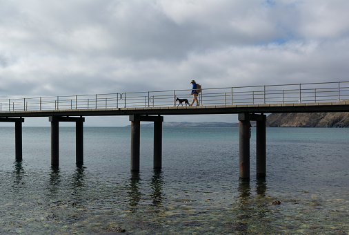 Rapid Bay, South Australia, Australia - May 5, 2018: Man and his dog walking out on the new cement jetty, perhaps for a day of fishing.