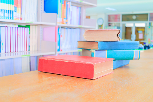 old book red - green. and heap treatise in school library on wooden table.  blurry bookshelves background. education learning concept with copy space add text