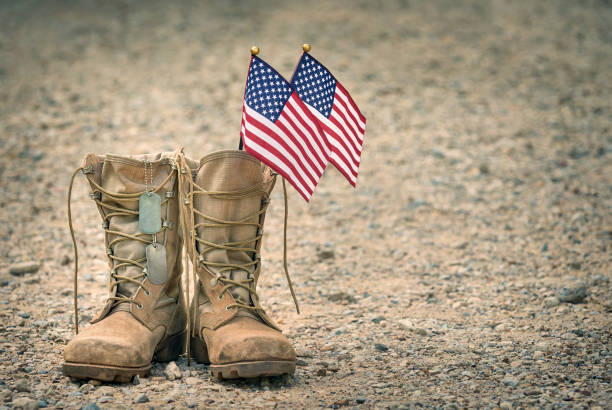 Old military combat boots with dog tags and the American flags Old military combat boots with dog tags and two small American flags. Rocky gravel background with copy space. Memorial Day or Veterans day concept. usa flag shoes stock pictures, royalty-free photos & images