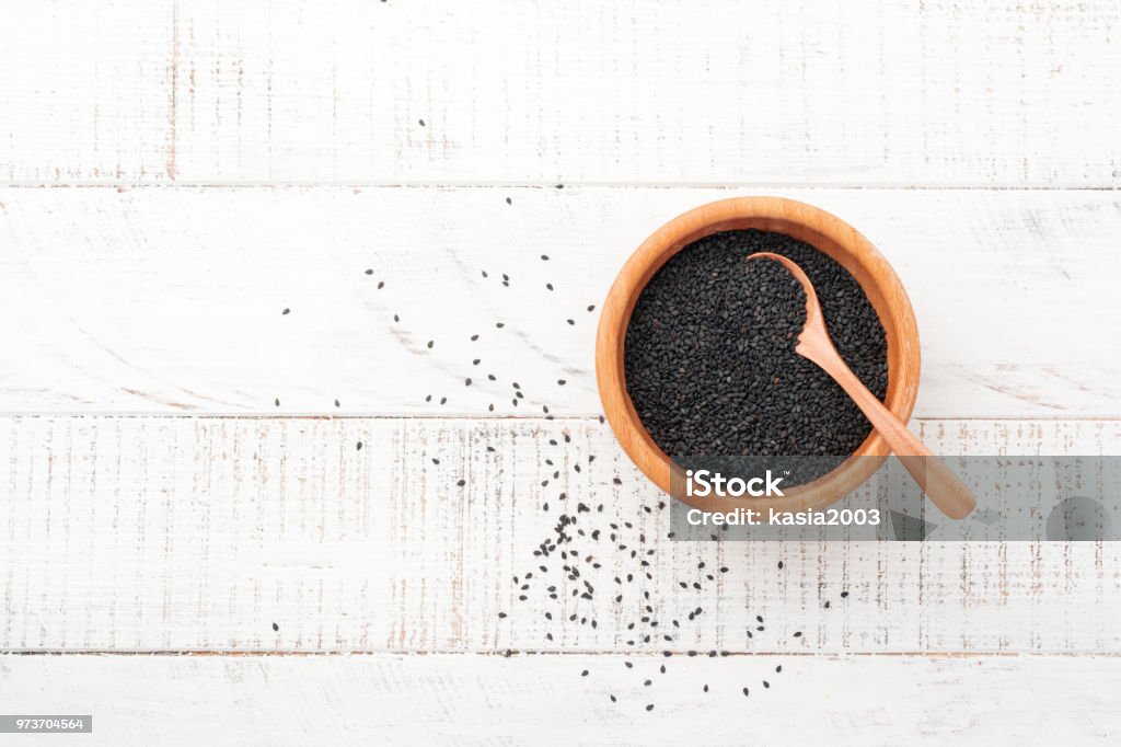Black sesame seeds in a bamboo bowl on white wooden background. Top view. Seed Stock Photo