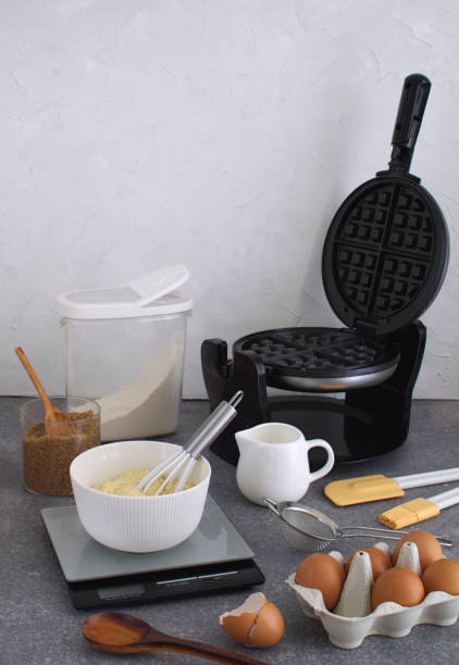 Cooking background of waffle preparation with batter, waffle iron, kitchen utensils and ingredients