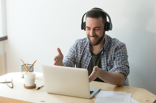 Smiling worker in headphones talking at laptop via video call