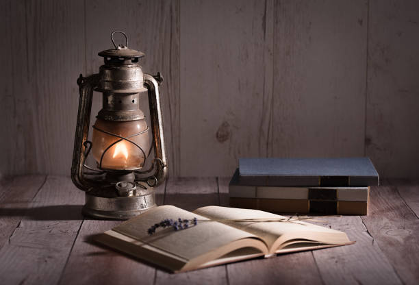 Old, antique book opened and burning kerosene lamp on wooden table