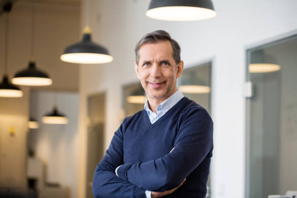 Confident mature businessman in office Portrait of a happy mature business professional standing with his arms crossed in modern office. Smiling businessman at his workplace. 55 59 years stock pictures, royalty-free photos & images