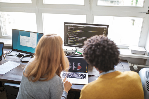 Rear view of male and female computer programmers working on a new project together in office. Software engineers working together at their desk.