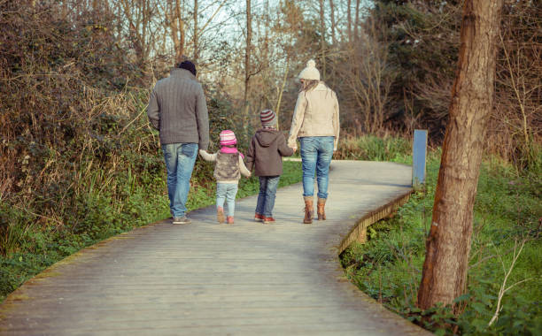 Happy family walking together holding hands in the forest Happy family walking together holding hands over a wooden pathway into the forest back to front stock pictures, royalty-free photos & images