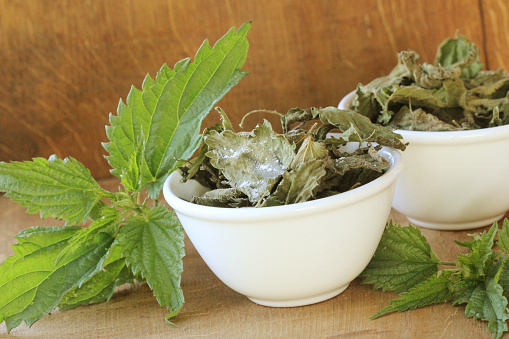 Stinging nettle chips in bowl and fresh nettle on table .
