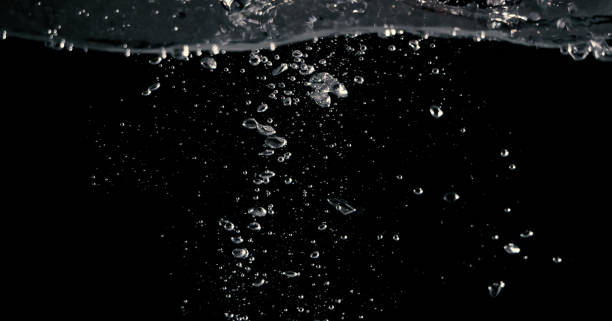 istock Soda water bubbles splashing and floating drop in black background 973761602