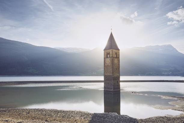 Old church tower in water at sunset. Resia Lake (Lago di Resia or Reschensee) in South Tyrol, Italy.