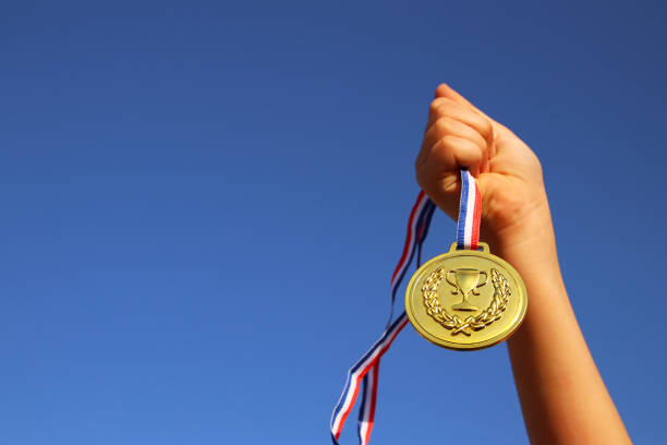 mão da criança gerada, segurando a medalha de ouro contra o céu. conceito de educação, sucesso, realização, prêmio e vitória. - medalist - fotografias e filmes do acervo