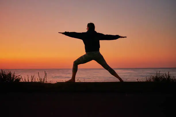 Woman silhouette practising yoga during the sunset by the sea