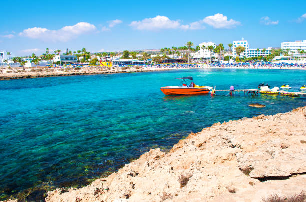 bild von einem roten schnellboot in der bucht von vathia gonia strand in der nähe von agia napa, zypern. felsige küste und meer mit türkisblauen wasser in einer bucht, häuser im hintergrund. warmer tag im herbst - scenics building exterior tourist resort orange stock-fotos und bilder