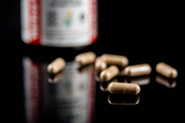 A bottle of ceylon cinnamon capsules with several of the dietary supplement capsules in front shot in studio against a black background on a reflective surface.