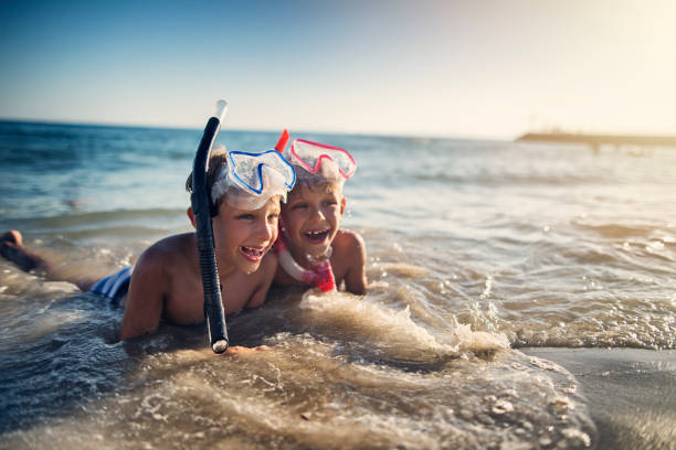 Little brothers got tired snorkeling. They are resting lying on the sand and being splashed by waves.\nSunny summer vacations day.\nNikon D810