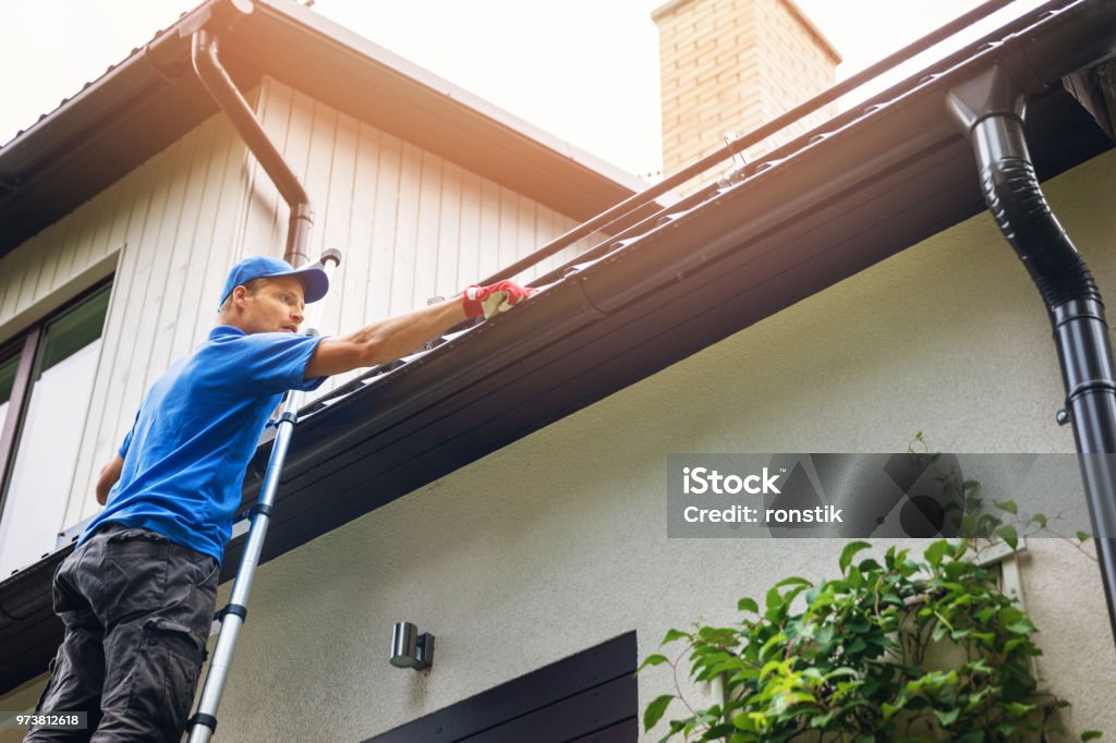 hombre en escalera limpiar canalón de la casa de las hojas y suciedad - Foto de stock de Canaleta del tejado libre de derechos