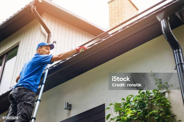 Hombre En Escalera Limpiar Canalón De La Casa De Las Hojas Y Suciedad Foto de stock y más banco de imágenes de Canaleta del tejado