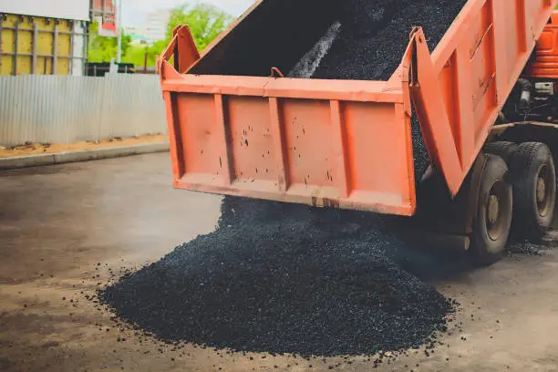 The truck unloads fresh asphalt into the spreader on the big road in the city