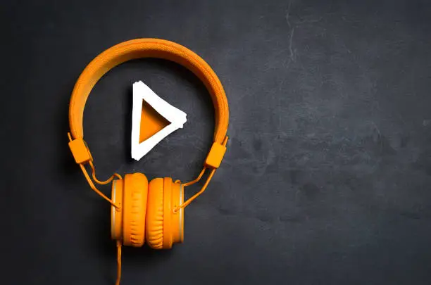 Play button and orange headphones on dark concrete background