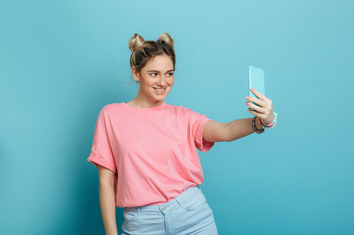 youth trendy woman making photo on her smartphone against a blue pastel background . making cool selfie