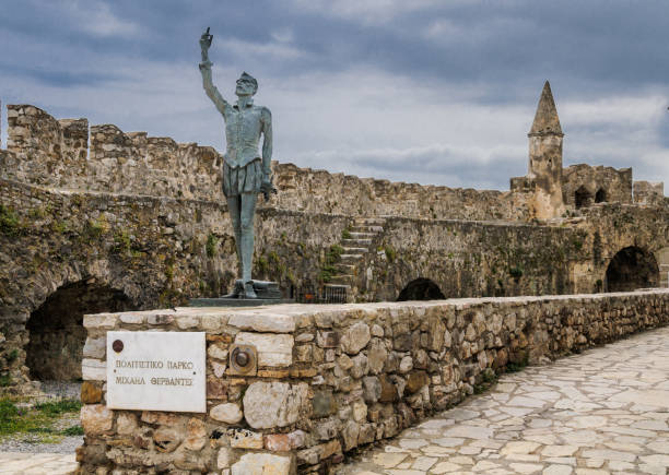 Nafpaktos,Greece-May 5, 2018- With the stone fort battlemernts of the harbor entrance as a backdrop a statue of Cervantes stands to memorialize the poet's participation in a  sea battle that took place here in 1571.