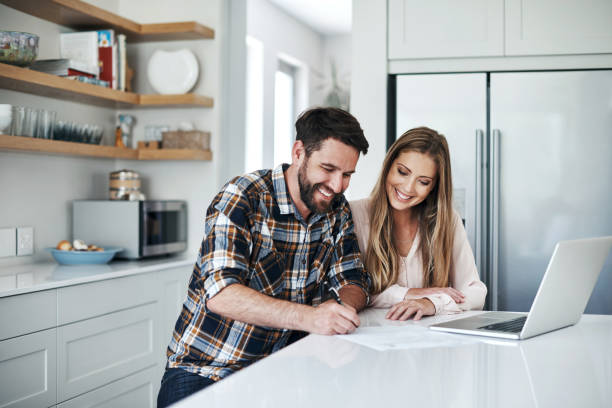 Budgeting is a breeze when it's done together Shot of a young couple using a laptop and going through paperwork at home young couple stock pictures, royalty-free photos & images