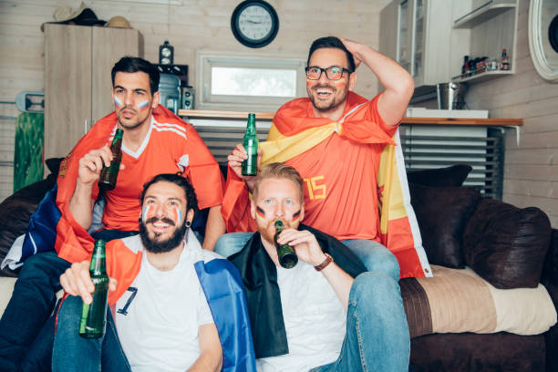 istock Men drinking beer and watching soccer game from home 973948018