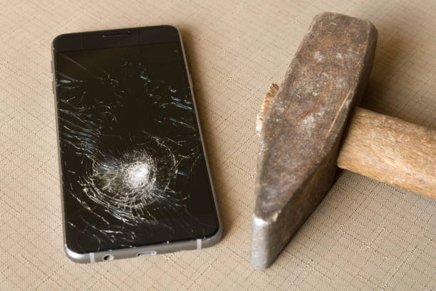 istock A broken cell phone and hammer on grey background 973949072
