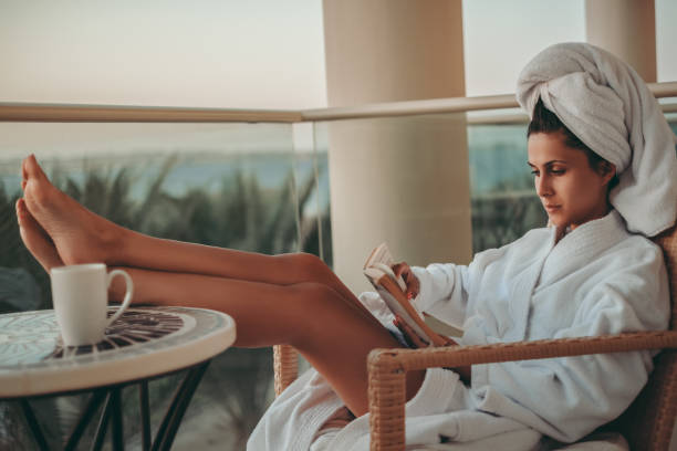 chica en bata de baño leyendo un libro en un balcón - bathrobe women cup towel fotografías e imágenes de stock