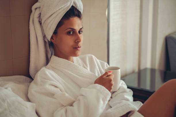 ragazza in accappatoio con asciugamano sui capelli che beve caffè - bathrobe women cup towel foto e immagini stock