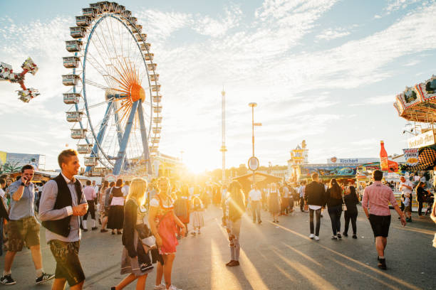 München, Deutschland - 29. September 2016: Besucher spazieren bei Sonnenuntergang über das Oktoberfestgelände, Riesenrad im Hintergrund.