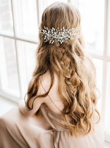 Portrait with natural light of pretty young woman with beautiful hairstyle decorated by stylish hair accessory, rear view