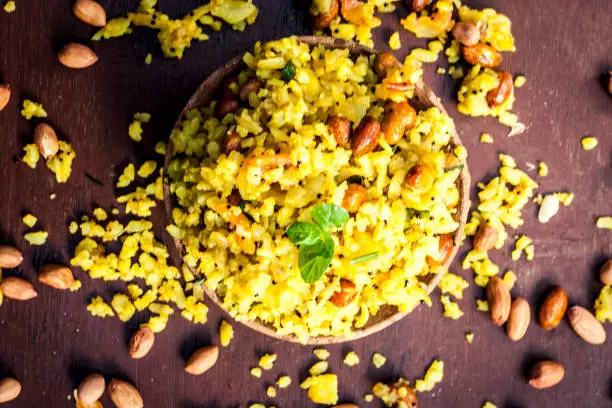 Close up of Indian popular brunch dish in a clay bowl with dried fried groundnut on it is Poha batata or Pava batata on a wooden surface in dark Gothic colors.