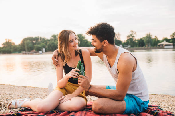 istock Happy couple sitting by the river and drinking beer 973998664