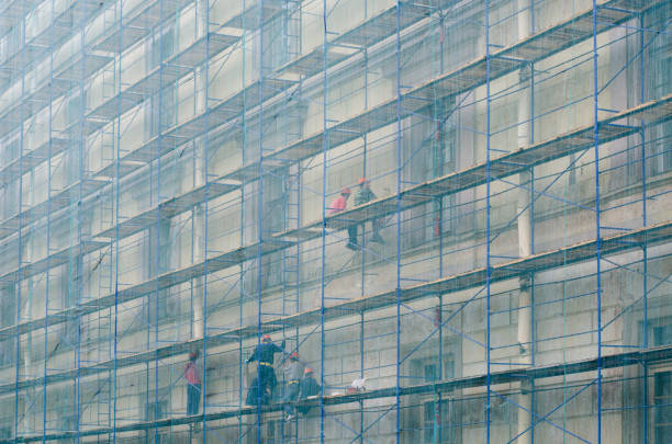 construtores sobre o andaime. reparação da fachada de um edifício de vários andares. - restoring house scaffolding history - fotografias e filmes do acervo