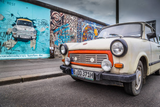 muro di berlino alla east side gallery con un vecchio trabant, il veicolo più comune utilizzato nella germania est, di fronte, berlino friedrichshain-kreuzberg, germania - east germany berlin germany graffiti wall foto e immagini stock