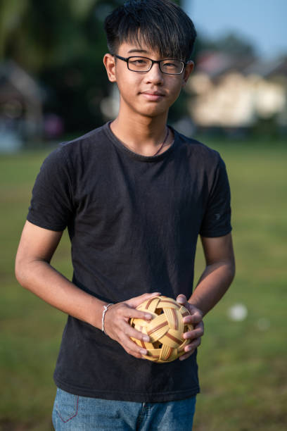 asian chinese teenage boy holding a sepak takraw in his hand looking in the camera - sepaktakraw imagens e fotografias de stock