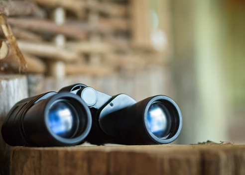 A pair of black binoculars on wooden table. A concept of exciting adventure and discovery.
