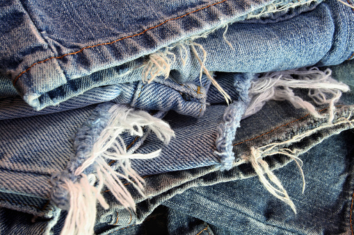 An abstract pile of several different pairs of ragged old blue jeans ready to be recycled.